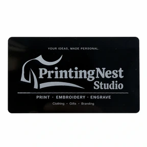 Glossy black metal business card with the PrintingNest Studio logo and silver-coloured engraved lettering on a white background